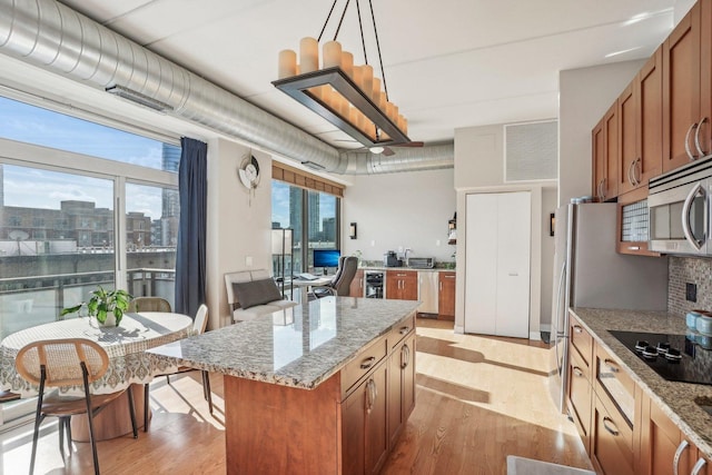 kitchen featuring light stone countertops, black electric cooktop, light hardwood / wood-style flooring, a center island, and hanging light fixtures