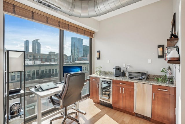 home office with light wood-type flooring and beverage cooler