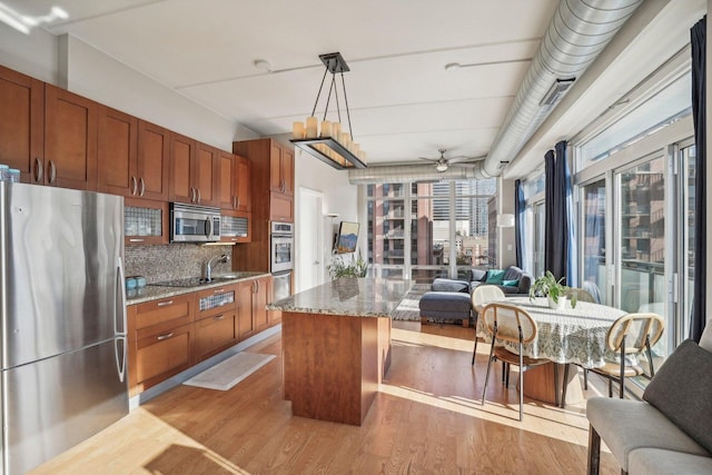 kitchen with light stone countertops, a center island, stainless steel appliances, backsplash, and decorative light fixtures