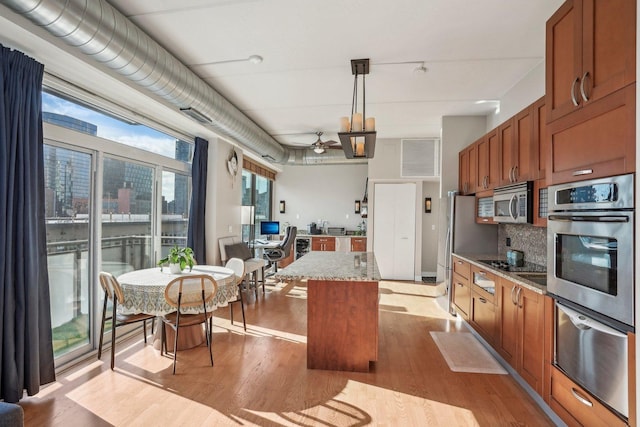 kitchen with a center island, hanging light fixtures, ceiling fan, light stone countertops, and stainless steel appliances