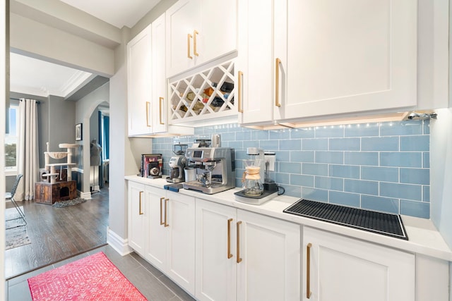 bar with tasteful backsplash, white cabinetry, crown molding, and dark tile patterned flooring