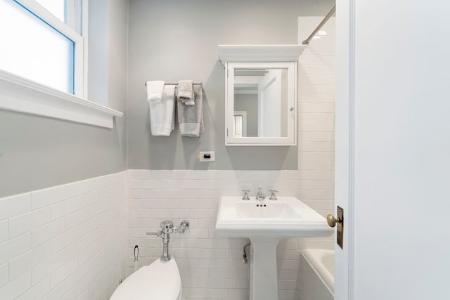 bathroom with a tub to relax in, toilet, and tile walls