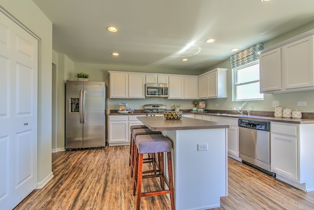 kitchen with white cabinets, a kitchen island, appliances with stainless steel finishes, and light hardwood / wood-style flooring