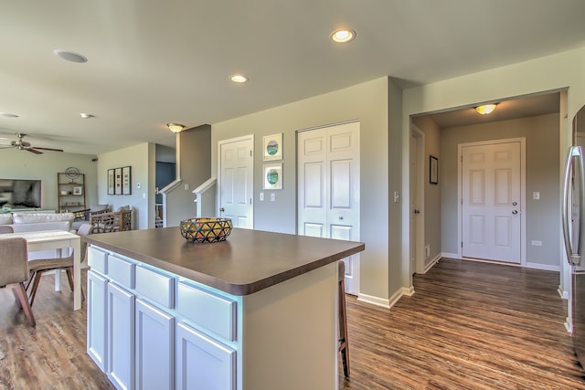 kitchen with white cabinets, ceiling fan, a kitchen island, dark hardwood / wood-style flooring, and stainless steel refrigerator