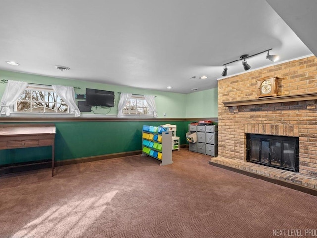 recreation room featuring carpet, track lighting, a wealth of natural light, and a brick fireplace