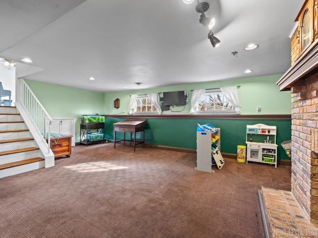 playroom with dark carpet, a brick fireplace, and ceiling fan