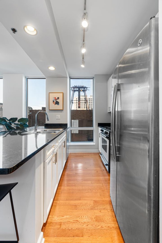 kitchen with gas stove, sink, light hardwood / wood-style flooring, stainless steel fridge, and white cabinets