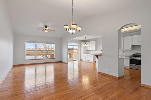 unfurnished living room featuring ceiling fan with notable chandelier, light hardwood / wood-style floors, and vaulted ceiling