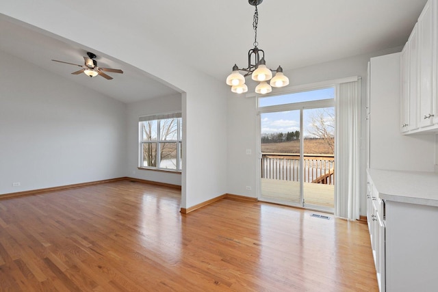 unfurnished dining area with lofted ceiling, plenty of natural light, ceiling fan with notable chandelier, and light hardwood / wood-style flooring