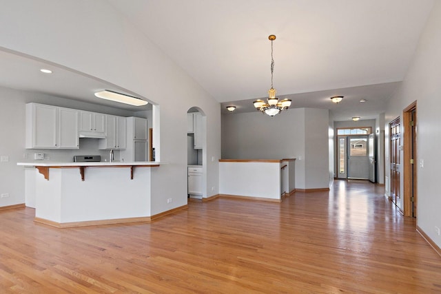 kitchen featuring hanging light fixtures, light hardwood / wood-style flooring, kitchen peninsula, a kitchen bar, and white cabinets