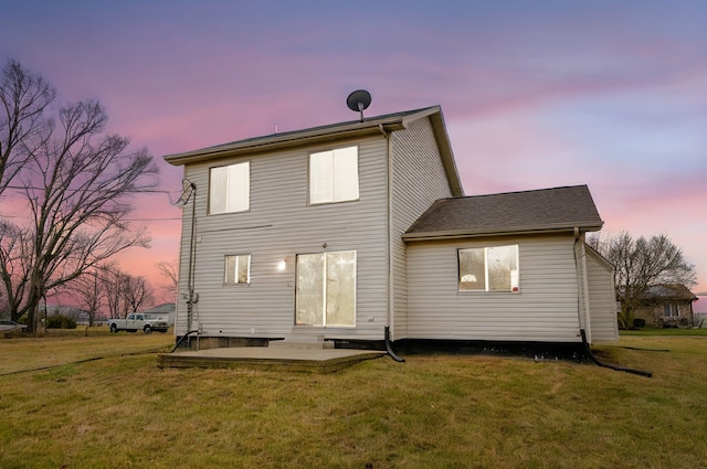 back house at dusk featuring a lawn and a patio