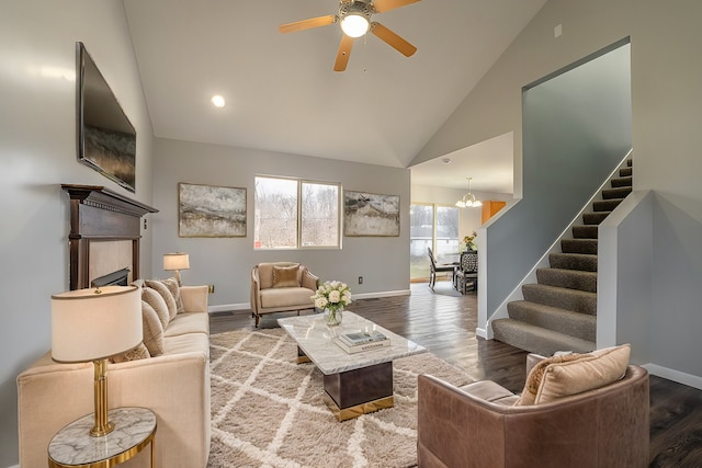 living room featuring hardwood / wood-style flooring, high vaulted ceiling, ceiling fan with notable chandelier, and a tile fireplace