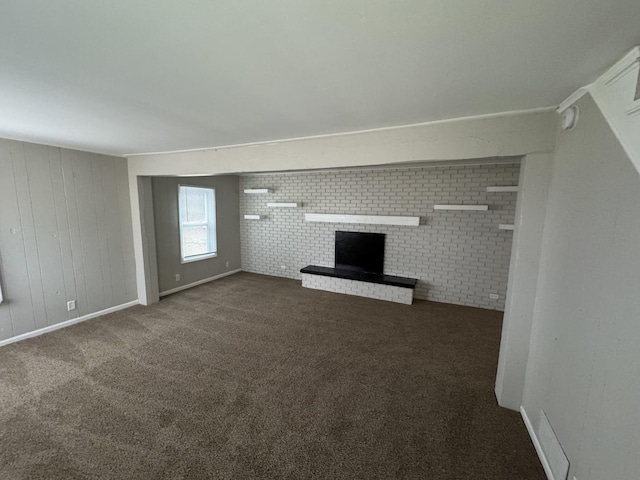 unfurnished living room with dark carpet, a fireplace, and brick wall