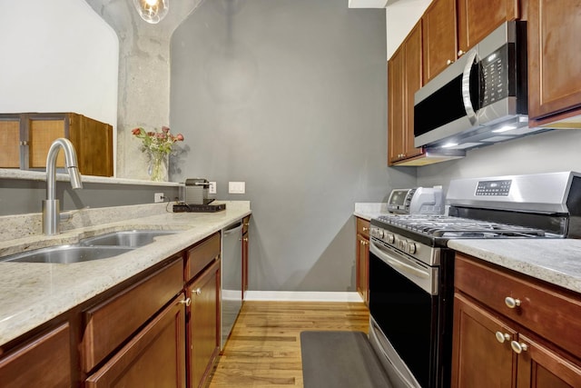 kitchen featuring light stone counters, sink, stainless steel appliances, and light wood-type flooring