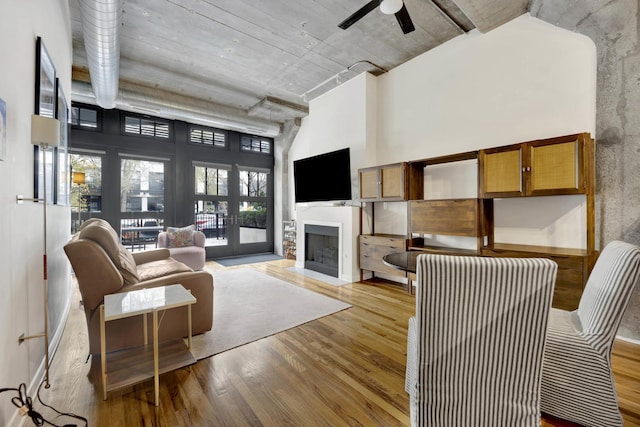 living room featuring ceiling fan, light wood-type flooring, a towering ceiling, and french doors