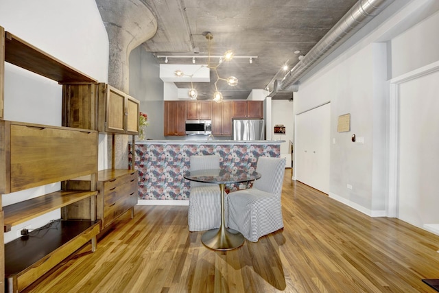 dining area with light hardwood / wood-style flooring, a high ceiling, and track lighting