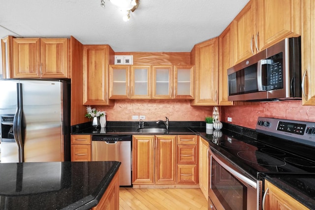 kitchen featuring sink, stainless steel appliances, dark stone countertops, a textured ceiling, and light wood-type flooring