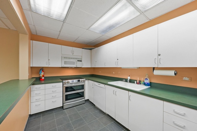 kitchen with a paneled ceiling, white cabinetry, white appliances, and sink