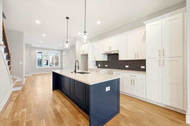 kitchen with a kitchen island with sink, sink, and white cabinets