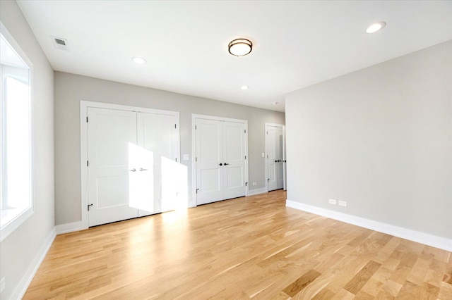 unfurnished bedroom featuring light hardwood / wood-style floors and two closets