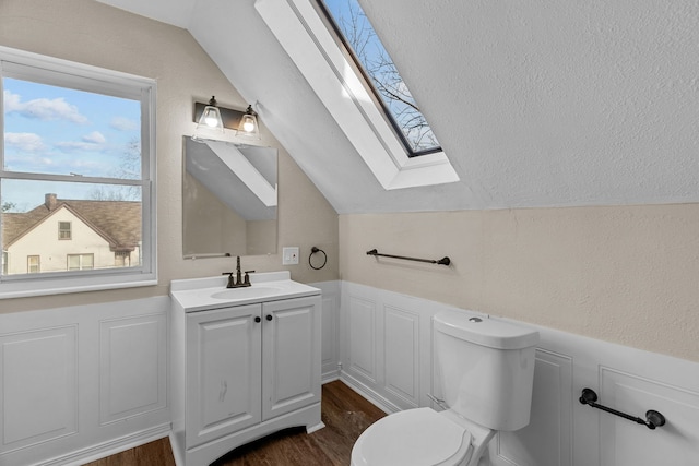 bathroom with hardwood / wood-style flooring, vanity, toilet, and lofted ceiling with skylight