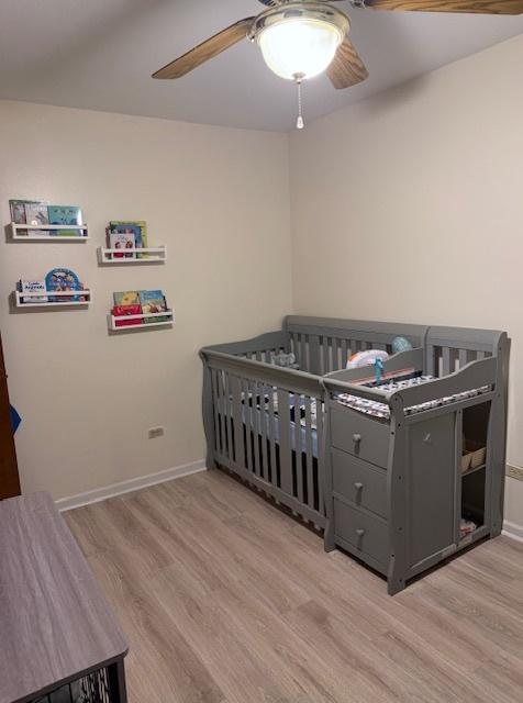 bedroom with ceiling fan, a nursery area, and light wood-type flooring