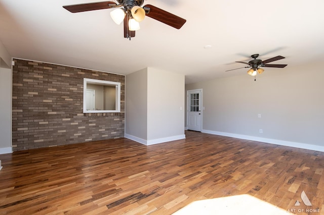 unfurnished living room with ceiling fan, brick wall, and wood-type flooring