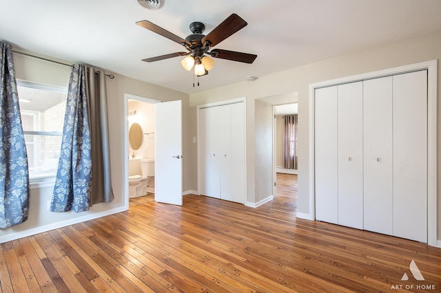 unfurnished bedroom with connected bathroom, multiple closets, a baseboard radiator, ceiling fan, and hardwood / wood-style floors