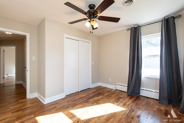 unfurnished bedroom featuring ceiling fan, a baseboard radiator, dark hardwood / wood-style floors, and a closet