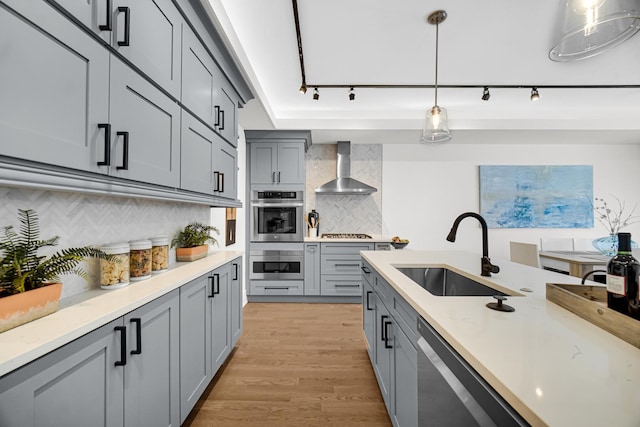 kitchen featuring pendant lighting, gray cabinets, appliances with stainless steel finishes, a sink, and wall chimney range hood