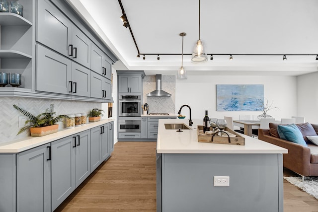 kitchen with stainless steel appliances, light countertops, a sink, and wall chimney range hood