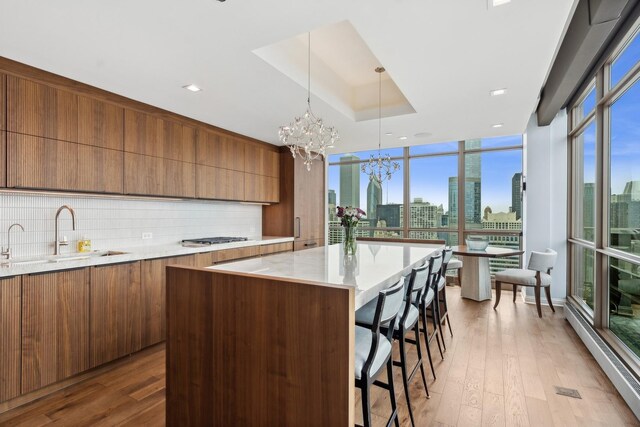 kitchen with a large island, sink, an inviting chandelier, pendant lighting, and light wood-type flooring