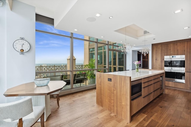 kitchen featuring floor to ceiling windows, stainless steel appliances, a chandelier, a center island, and light hardwood / wood-style floors