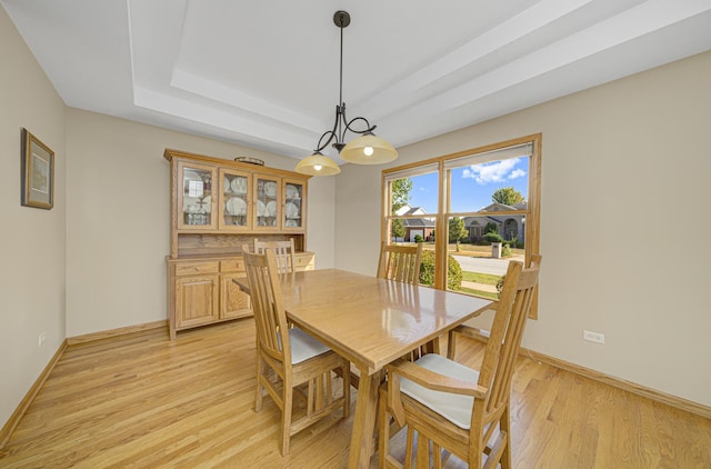 dining area with a raised ceiling and light hardwood / wood-style flooring