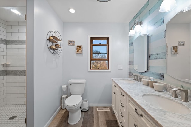 bathroom featuring wood-type flooring, a tile shower, vanity, and toilet