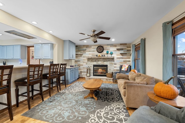 living room featuring ceiling fan, light wood-type flooring, and a fireplace