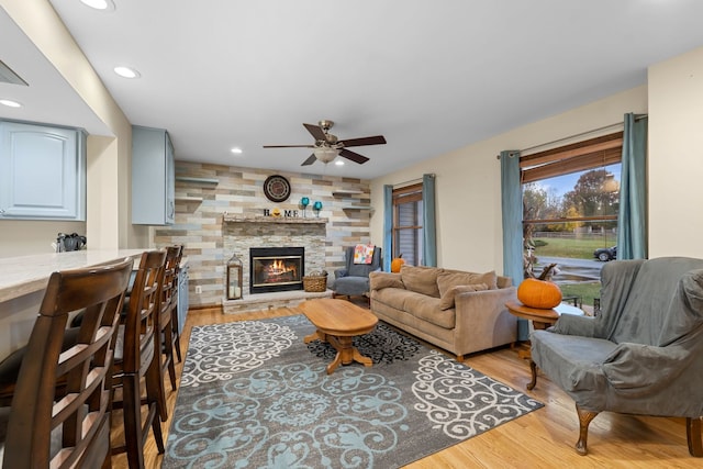 living room featuring ceiling fan, a fireplace, and light wood-type flooring