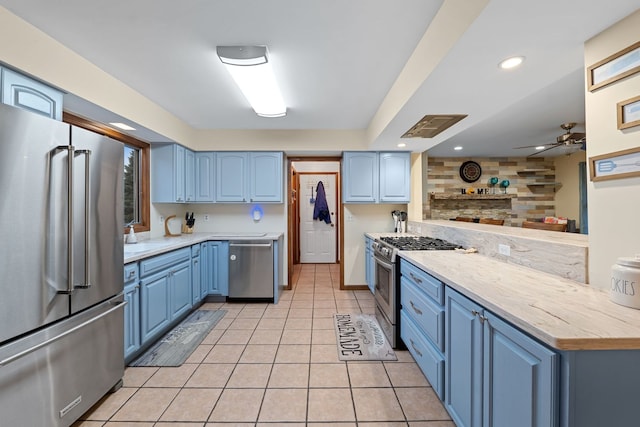 kitchen featuring blue cabinetry, high end appliances, light tile patterned floors, kitchen peninsula, and ceiling fan