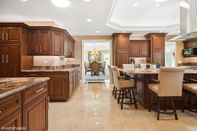 kitchen featuring a kitchen breakfast bar, island range hood, a tray ceiling, and an inviting chandelier