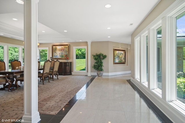 hallway featuring decorative columns, light tile patterned floors, and ornamental molding