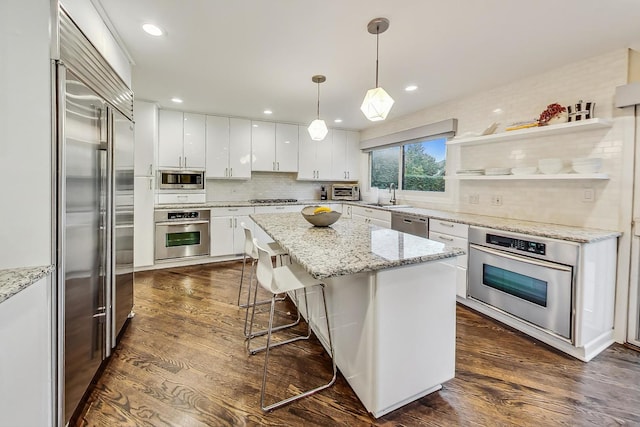 kitchen with a breakfast bar, built in appliances, white cabinets, a kitchen island, and hanging light fixtures