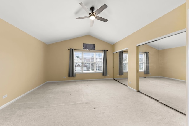 unfurnished bedroom with ceiling fan, vaulted ceiling, light carpet, and multiple closets