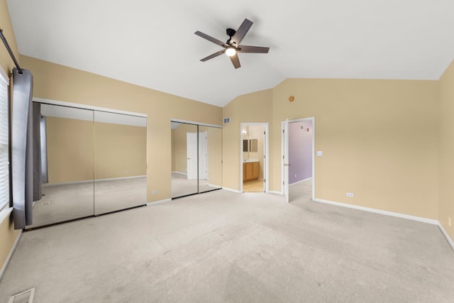 unfurnished bedroom with lofted ceiling, two closets, ensuite bath, ceiling fan, and light colored carpet