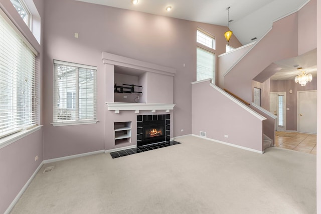 unfurnished living room featuring a notable chandelier, carpet floors, high vaulted ceiling, and a tiled fireplace