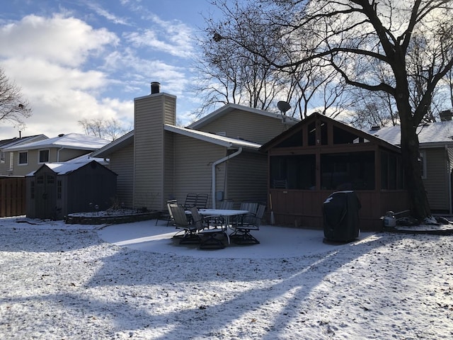 snow covered rear of property featuring a sunroom