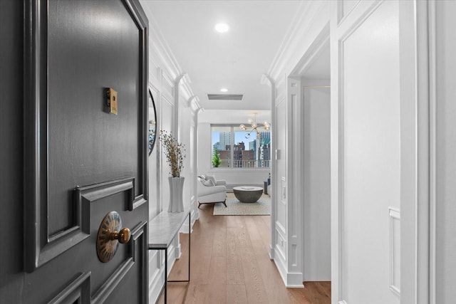 hall featuring a notable chandelier, light hardwood / wood-style floors, and ornamental molding