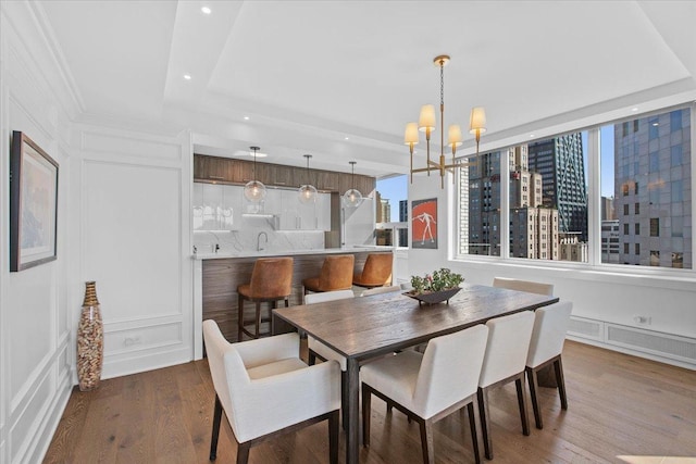 dining room with a raised ceiling, wood-type flooring, sink, and an inviting chandelier