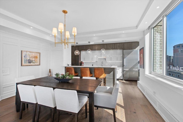 dining room with a tray ceiling, sink, dark hardwood / wood-style flooring, and an inviting chandelier