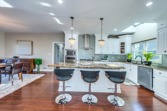 kitchen featuring a center island, white cabinets, wall chimney exhaust hood, appliances with stainless steel finishes, and decorative light fixtures