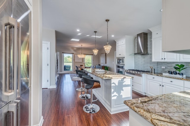 kitchen with appliances with stainless steel finishes, light stone counters, wall chimney exhaust hood, white cabinets, and a center island